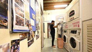A laundry room with multiple washing machines, a drying machine, and a person hanging clothes. - Poolside By Mingle (Kuala Lumpur)