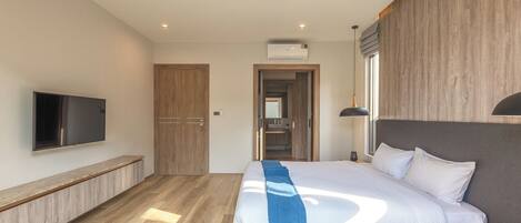 A modern hotel room with a large bed, a flat-screen TV, a wooden bench, and a view of the bathroom.