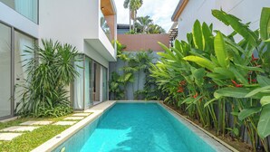 A modern pool area with a clear blue pool, surrounded by lush tropical plants and a contemporary building with large windows. - Near Beach & Famous Boat Ave V217 (Choeng Thale)