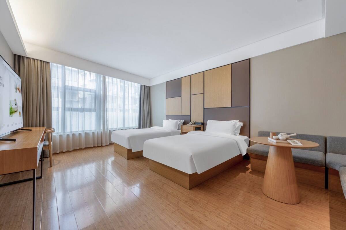 Una habitación de hotel moderna con dos camas, un escritorio, una mesa redonda y un ventanal con cortinas.