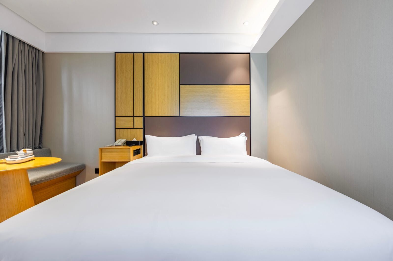 A modern hotel room with a large bed, a bedside table with a lamp, a small desk, and a chair.