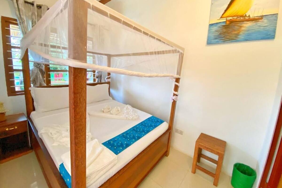 Una habitación con una cama de madera con dosel, un taburete pequeño y un cubo de basura verde.