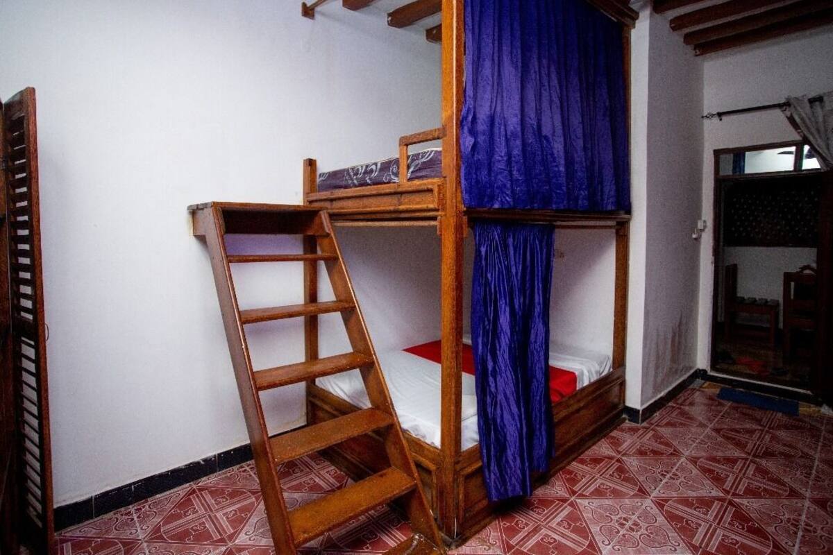 Una cama litera con escalera de madera, cortina azul y suelo estampado.