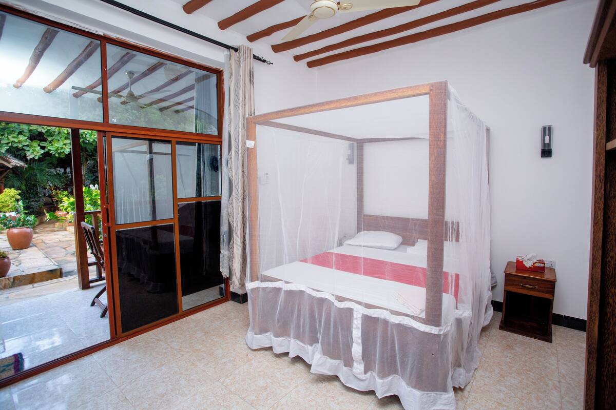 Un dormitorio con cama con dosel, puertas corredizas a un patio y una mesita de noche pequeña.