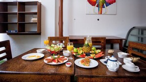 A wooden dining table with breakfast items, a fruit bowl, and a painting of an elephant on the wall.