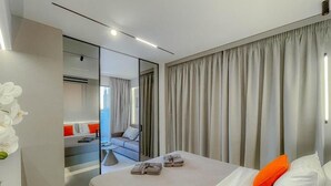 Ein modernes Hotelzimmer mit einem großen Bett, einem Spiegel, einer Sitzecke inklusive Sofa und Sesseln sowie Blick ins Freie.