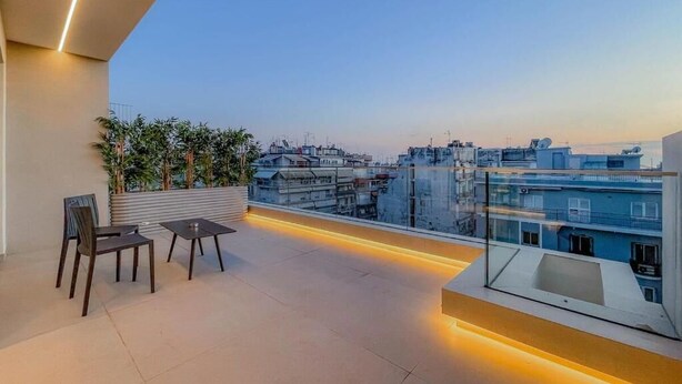 Eine Dachterrasse mit Sitzgelegenheit, Glasgeländer und Blick auf die Stadt.