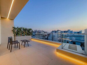 Une terrasse sur le toit, dotée d’un espace salon, d’une balustrade en verre et offrant une vue sur le paysage urbain.