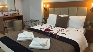 A hotel room with a neatly made bed, a bedside table with a lamp, a small plant, and a trash bin. - Novostar Otel (Edirne)