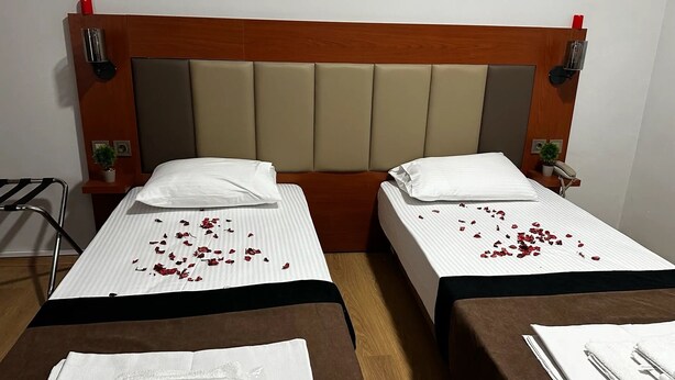 A hotel room with two single beds, each with a white pillow and a brown bedspread. There are rose petals scattered on the beds. - Novostar Otel (Edirne)