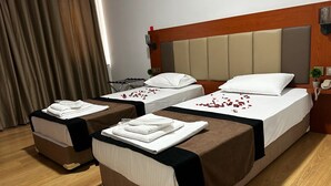 Quarto de hotel com duas camas, cada uma com cabeceira, e uma mesinha com toalhas.