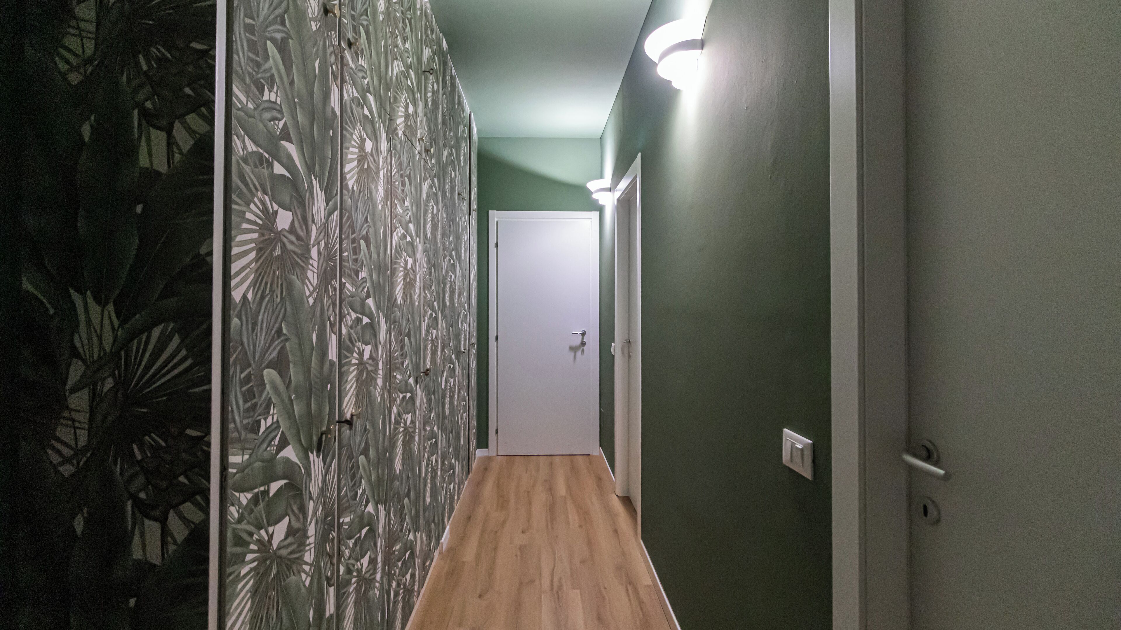 A hallway with a wooden floor, green walls, and a door at the end.
