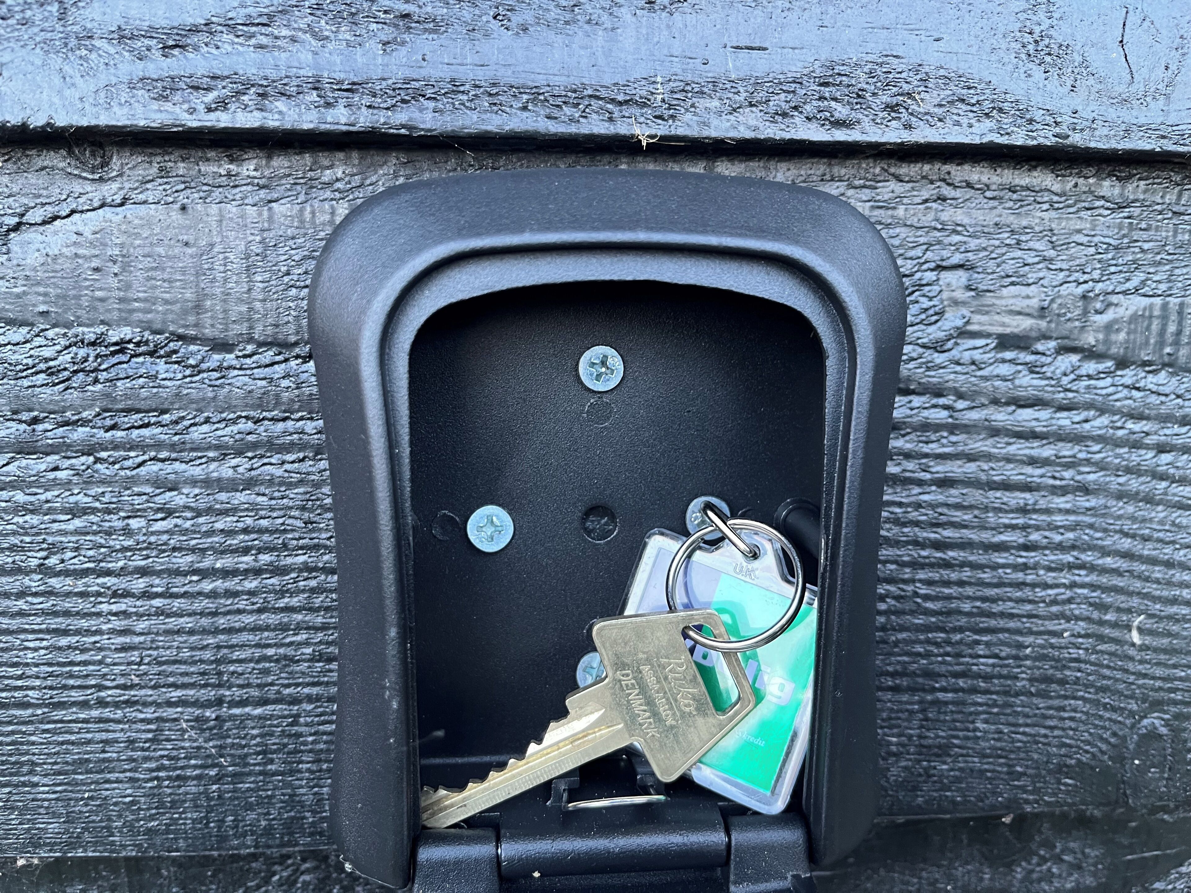 A black metal box with a key slot, two keys, and a keychain with a UK tag.