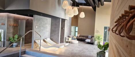 A modern indoor pool area with a seating area, lounge chairs, and a staircase leading to the pool.