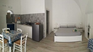 Een compacte kamer met een kitchenette, een eettafel met stoelen, een bed en een kledingkast.