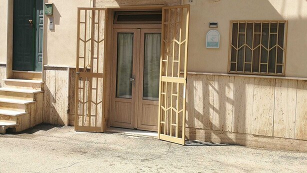 Una entrada de edificio con puerta de madera, un ventanal con barrotes y una escalera que sube.