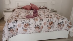 Una cama bien hecha con una colcha estampada, dos almohadas y una toalla doblada. Hay dos mesitas de noche con lámparas.