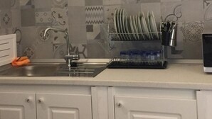 Una cocina con lavamanos, escurreplatos y utensilios.