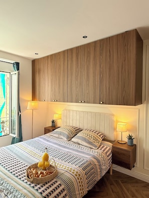 A bedroom with a bed, bedside lamps, a window, and a wall unit.