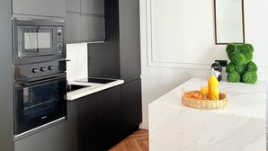 A modern kitchen with dark cabinetry, a microwave, oven, and a marble countertop. - Charming 2-room apartment with balcony (Nice)