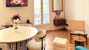 A living room with a fireplace, a round dining table, a sofa, a chair, and a small side table with a plant. - Charming 2-room apartment with balcony (Nice)