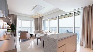 Una cocina moderna con una isla de mármol, un comedor con una mesa y sillas blancas, y grandes ventanales con vistas a la ciudad.