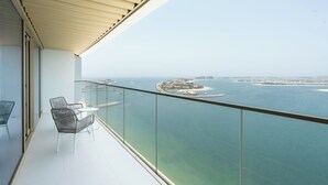 Un balcón con barandilla de vidrio que ofrece vistas a una ciudad costera, aguas cristalinas y islas a lo lejos.