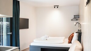 A modern hotel room with a bed, a small round table, a sofa, a TV mounted on the wall, and a window with curtains.