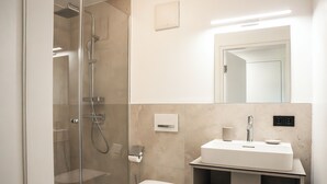 A modern bathroom with a glass-enclosed shower, a toilet, a sink with a mirror above it, and a towel rack.