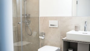 A modern bathroom with a glass-enclosed shower, a toilet, and a sink with a mirror above.