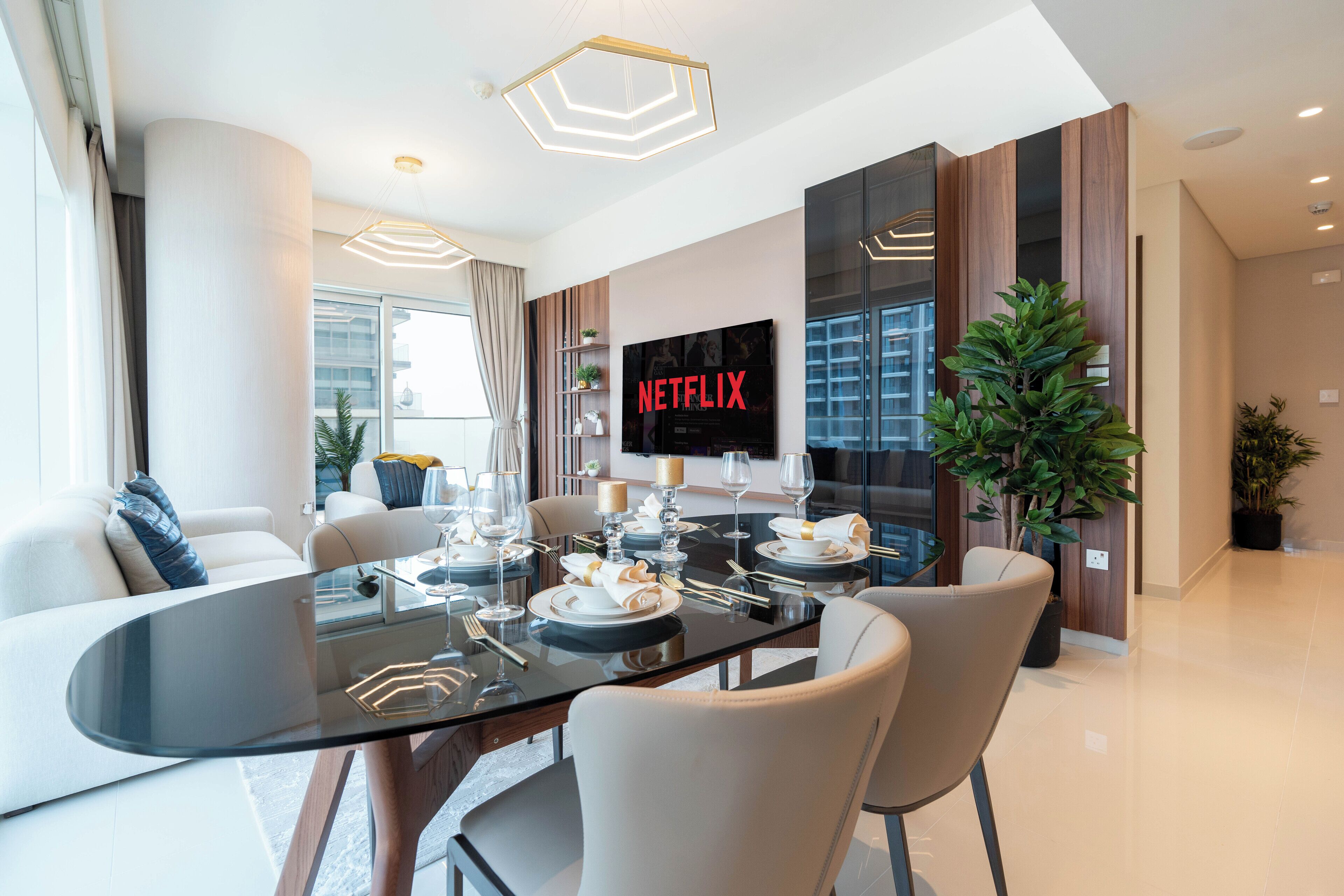 Un espace repas moderne avec une table en verre, des chaises blanches et un téléviseur diffusant du contenu « NETFLIX ».