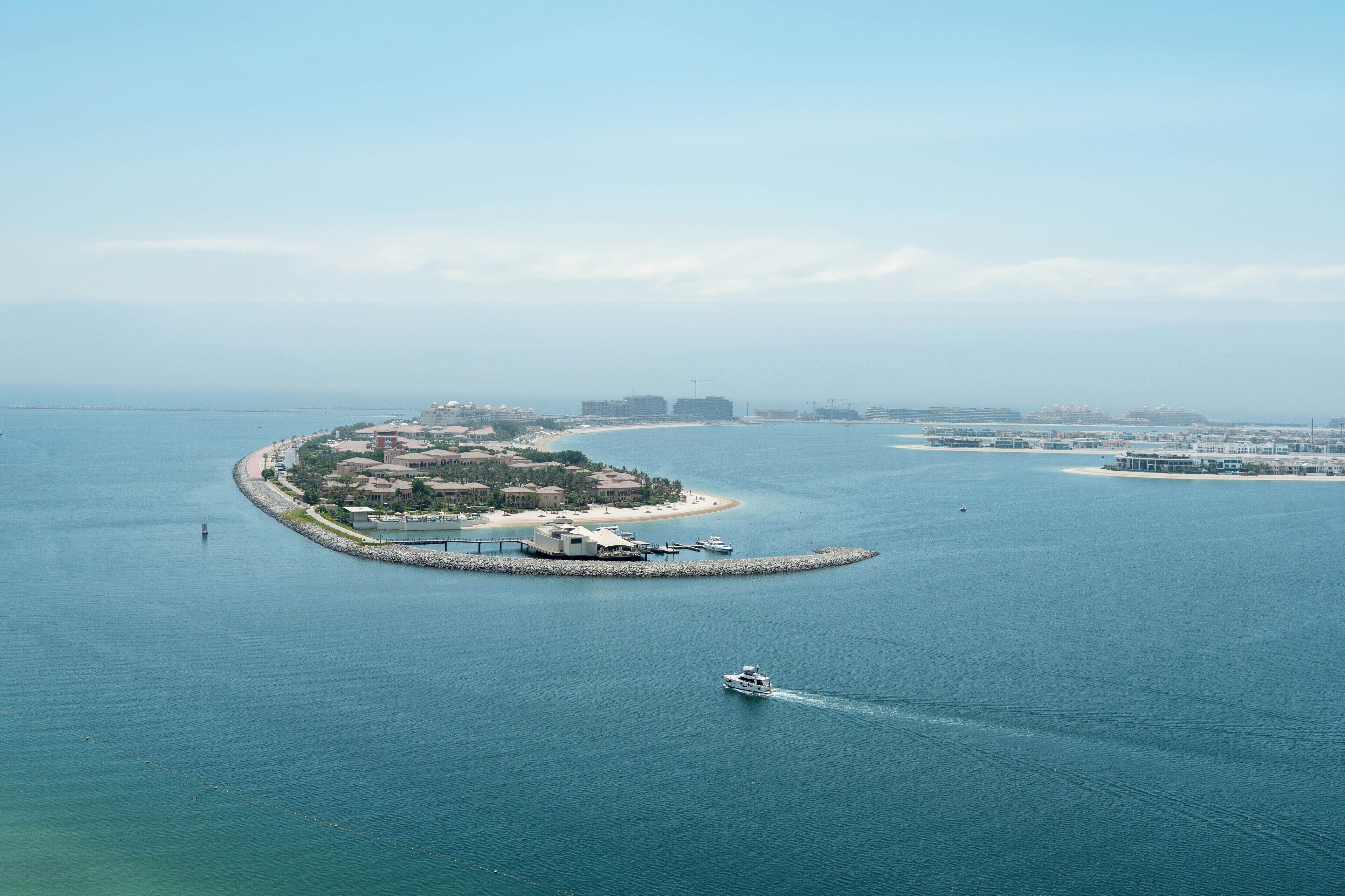 An aerial view of a coastal resort with a marina, a small island with buildings, and a clear blue sea.