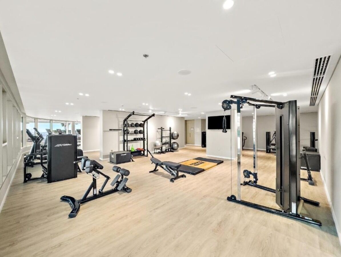 A modern gym with various exercise equipment, a wooden floor, and a large mirror.
