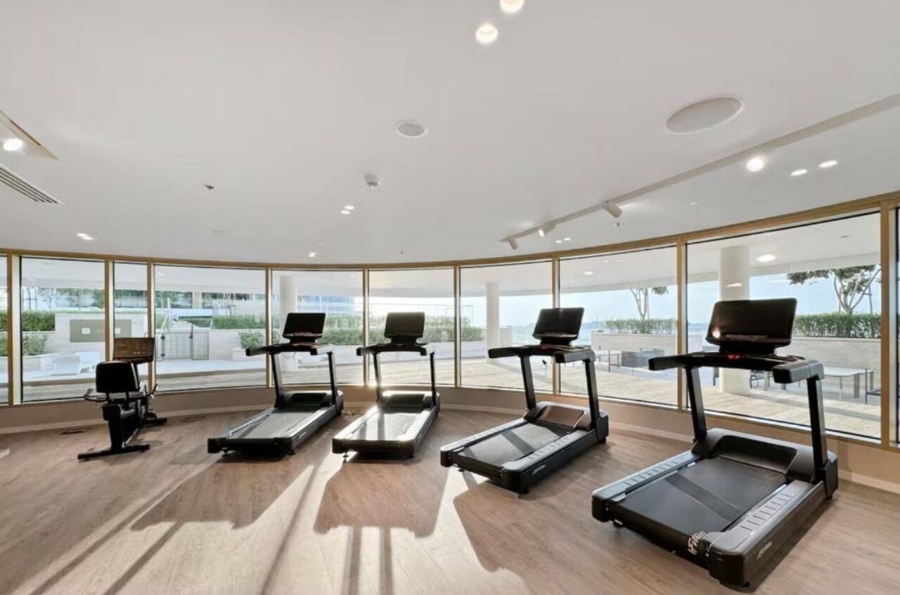 Un gimnasio con cuatro cintas de correr, ventanas amplias y vistas al exterior.