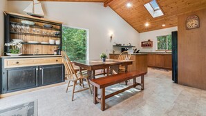 Un vaste espace dédié à la salle à manger, avec une table et des bancs en bois, une bibliothèque intégrée et une vue sur l’extérieur.