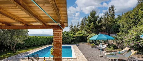 Area piscina con sedie a sdraio e un tavolo, immersa nel verde sotto un cielo sereno.
