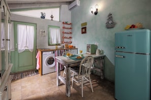 A compact kitchen with a washing machine, a dining table with chairs, a teal refrigerator, and a window with curtains. - Tiny House With Private Pool Kostrena (Kostrena)