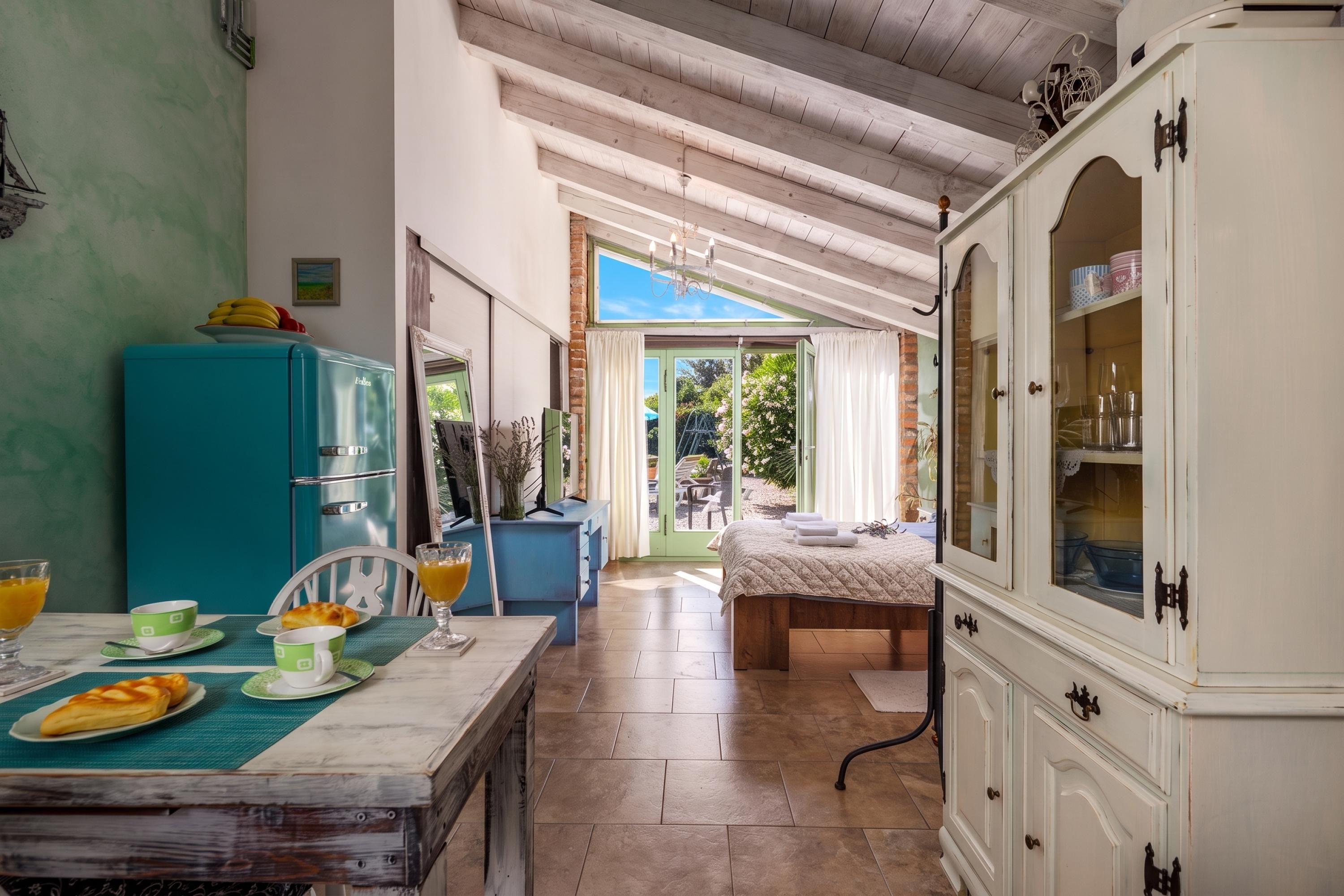 A cozy kitchen with a dining table set for breakfast, a blue refrigerator, and a view into the adjacent room.