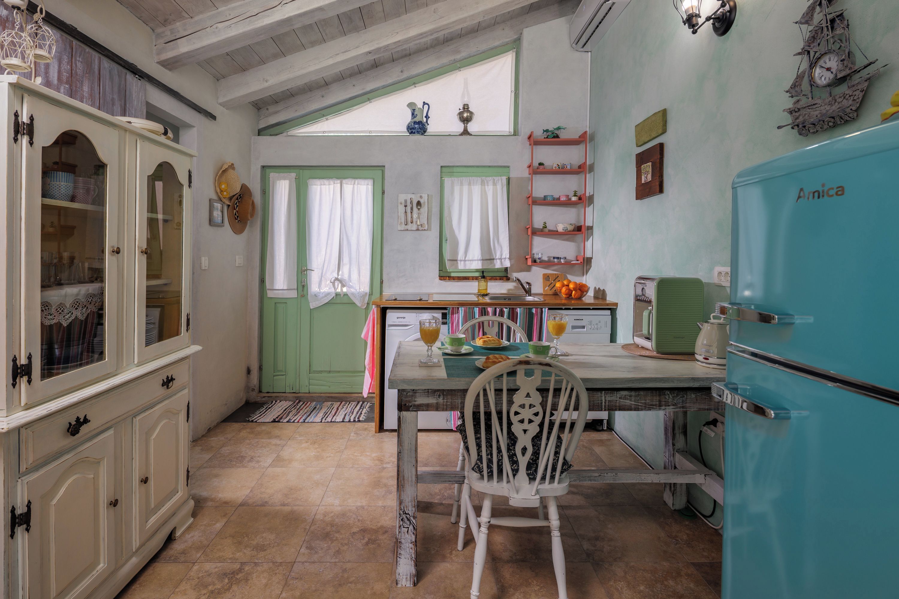 Una cocina con una mesa de comedor, sillas, un refrigerador y una ventana con cortinas.