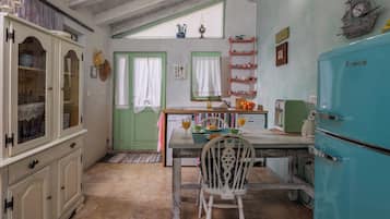 Una cocina con una mesa de comedor, sillas, un refrigerador y una ventana con cortinas.