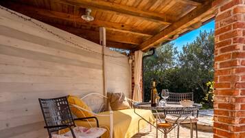 A covered outdoor seating area with a table, chairs, and a bottle of wine.