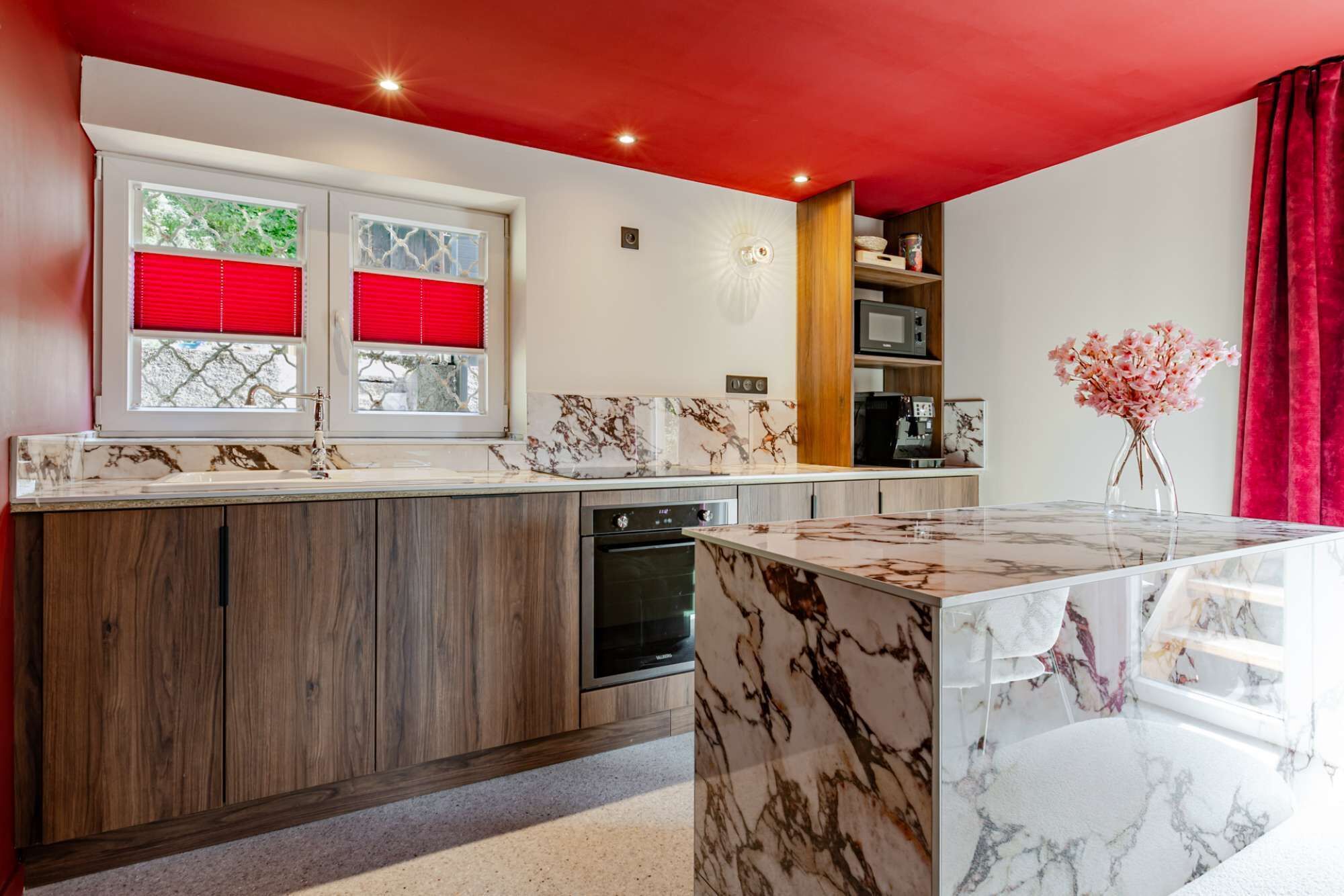 Een moderne keuken met een marmeren eiland, houten kastjes en rode details.