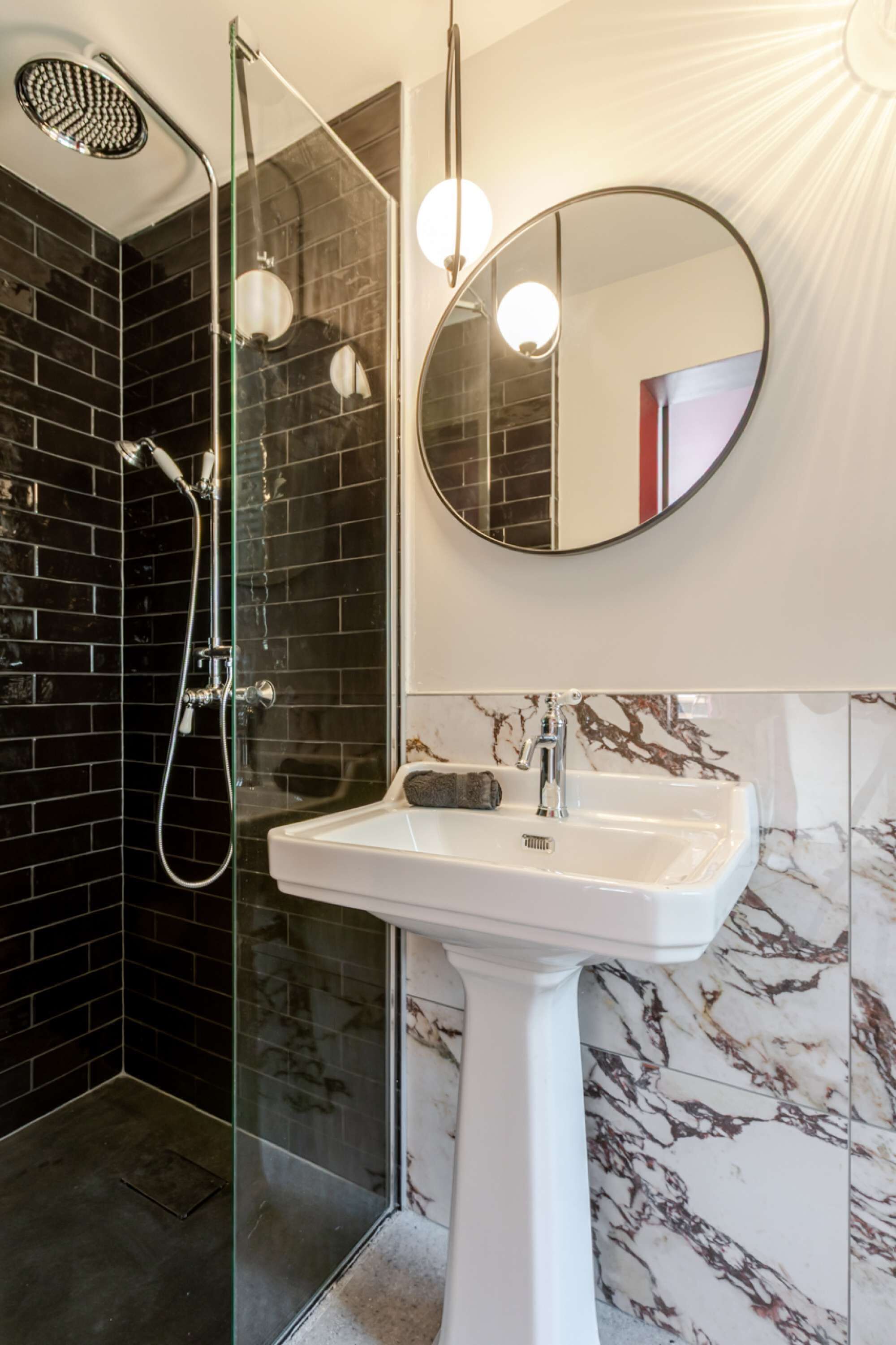 Une salle de bain moderne avec une douche à parois de verre, un lavabo sur colonne blanc et un miroir rond.
