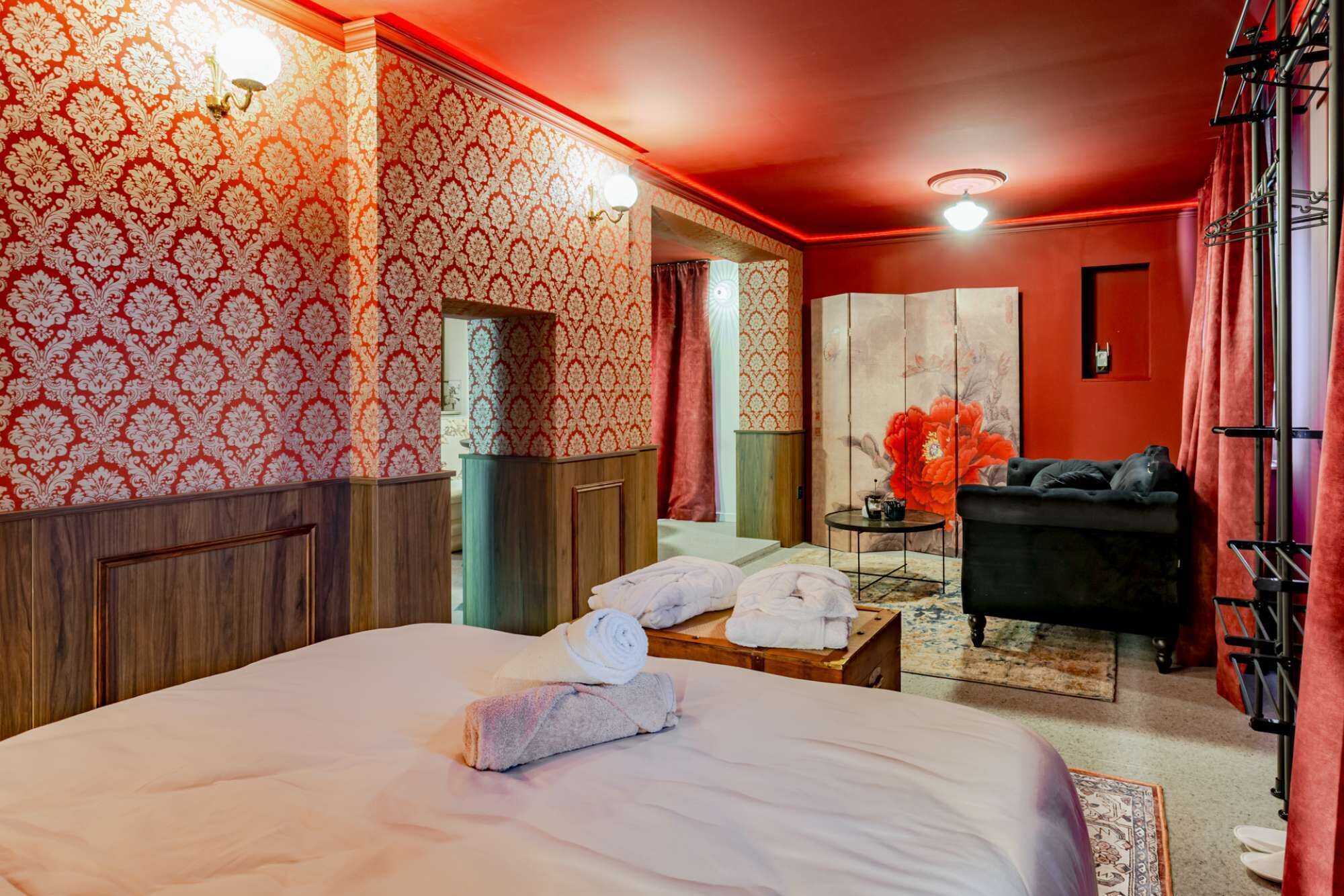 Ein Hotelzimmer mit einem großen Bett, einem kleinen Tisch mit Handtüchern, einer schwarzen Couch und einer roten Akzentwand.