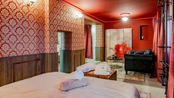 Ein Hotelzimmer mit einem großen Bett, einem kleinen Tisch mit Handtüchern, einer schwarzen Couch und einer roten Akzentwand.