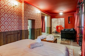 Hotellihuone, jossa on suuri sänky, pieni pöytä pyyhkeineen, musta sohva ja punainen tehosteseinä.