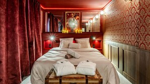 A hotel room with a large bed, red curtains, a wooden headboard, and a suitcase on the floor.