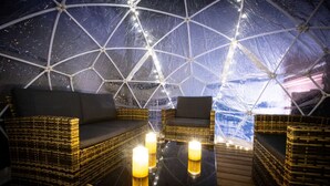 A geodesic dome structure with wicker furniture and candles on a wooden floor.