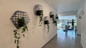 A hallway with hexagonal wall planters containing green plants, a tiled floor, and a view of the outside through large windows.