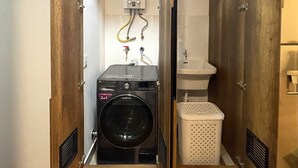 A compact, single-room bathroom with a built-in washer and dryer, a sink, and a small laundry basket.